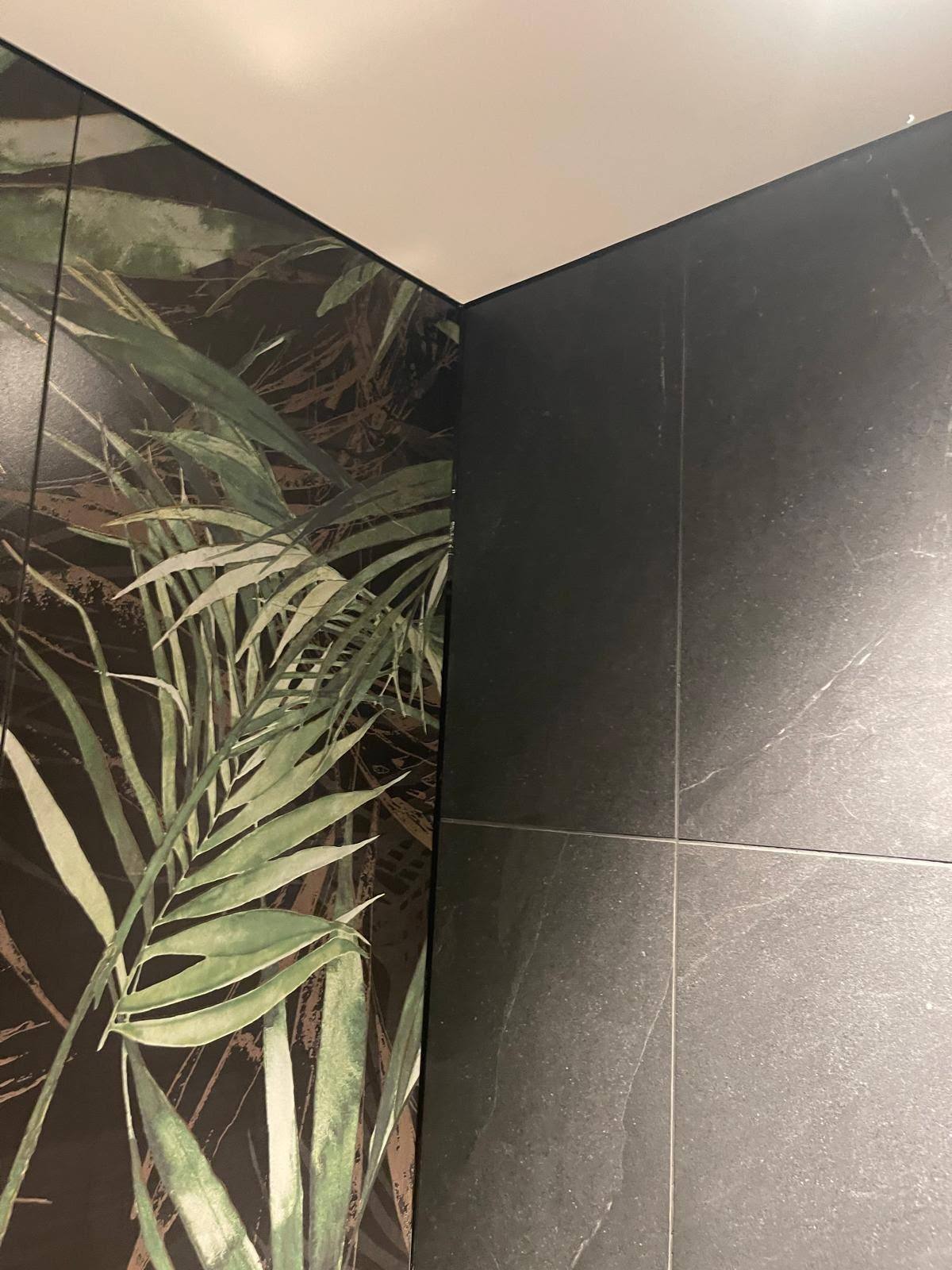 Sealed corner joint between wallpaper and dark grey bathroom wall tiles