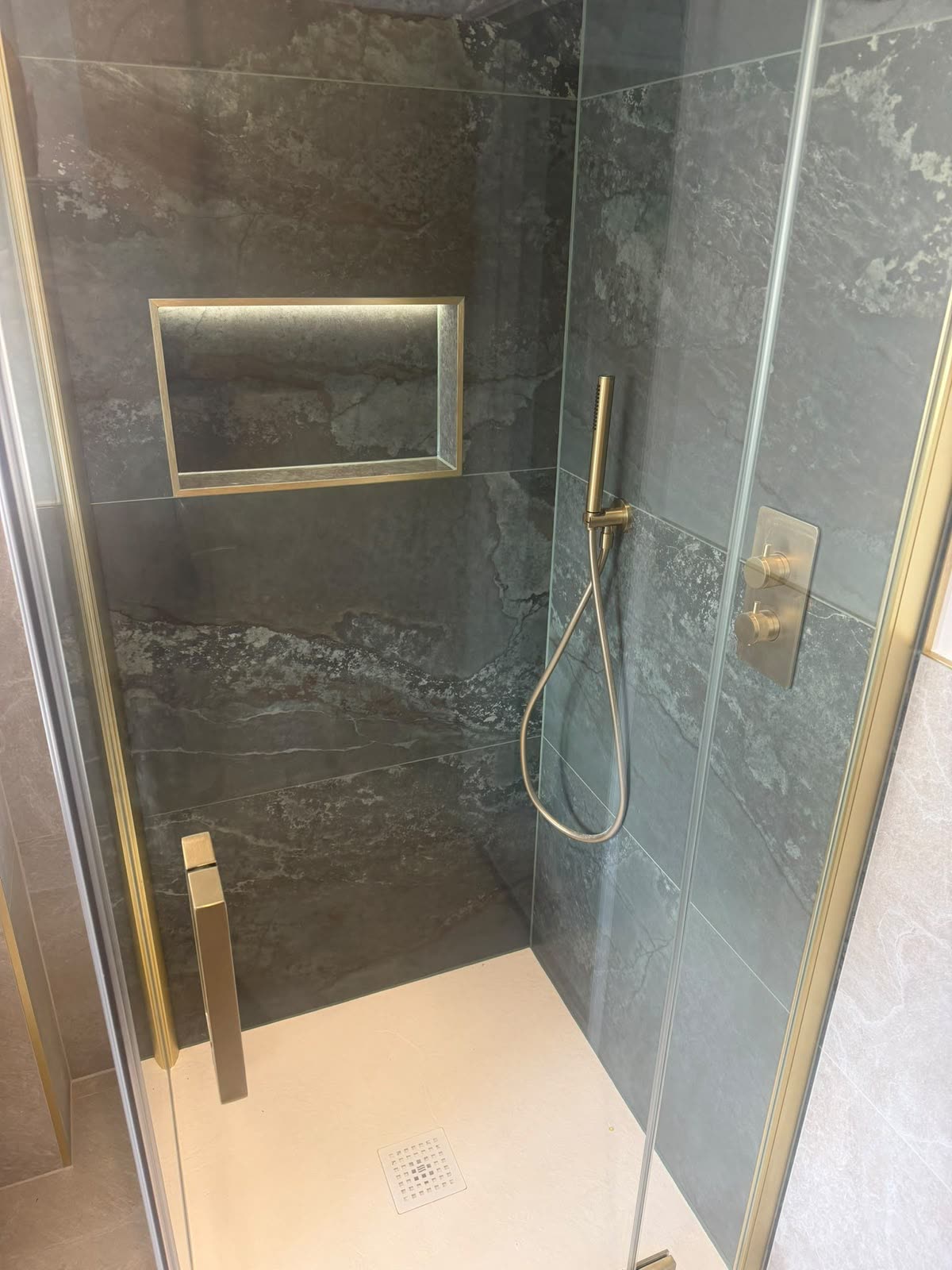 Dark stone shower enclosure with brass fittings and shower tray sealed with white silicone
