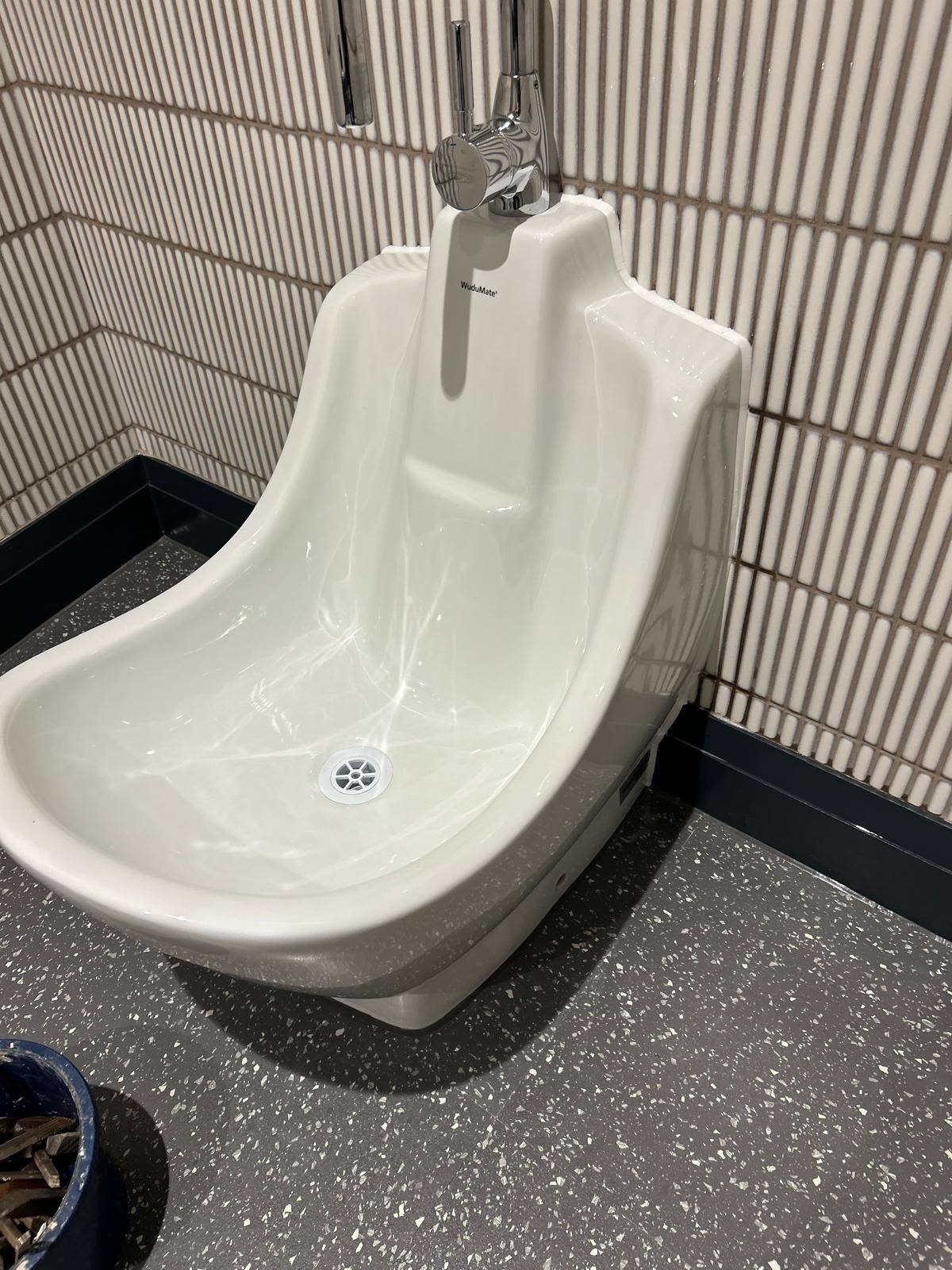 Ceramic foot wash station sealed to tiled walling in a commercial washroom