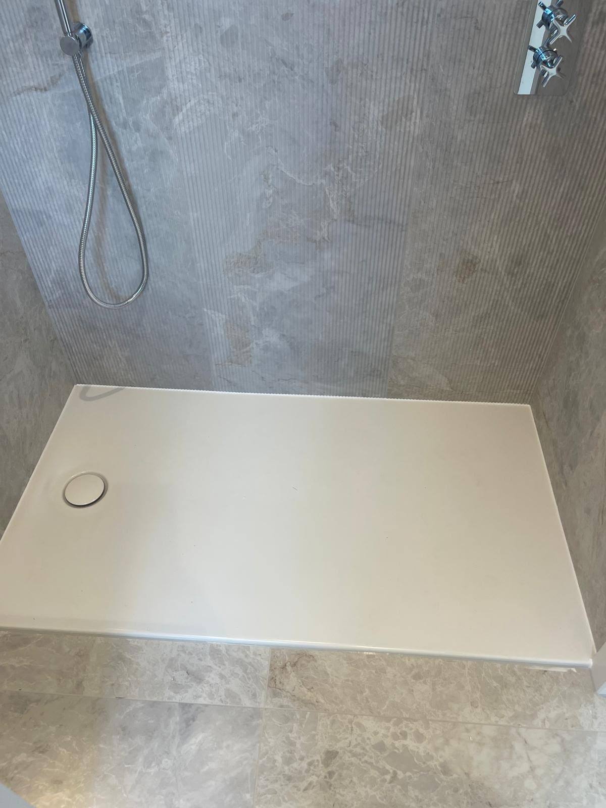 Shower tray sealed to grey textured wall tiles with a crisp silicone bead