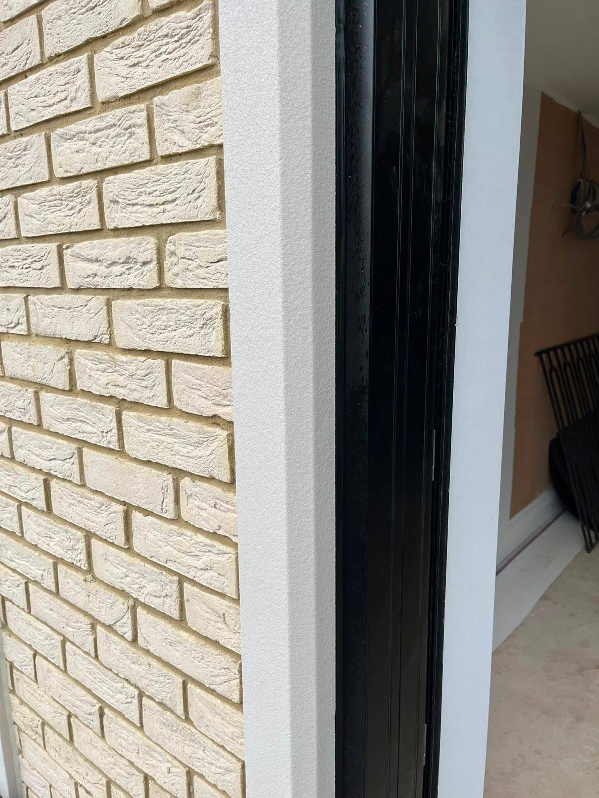 Weatherproof external sealant joint between a black door frame and brickwork