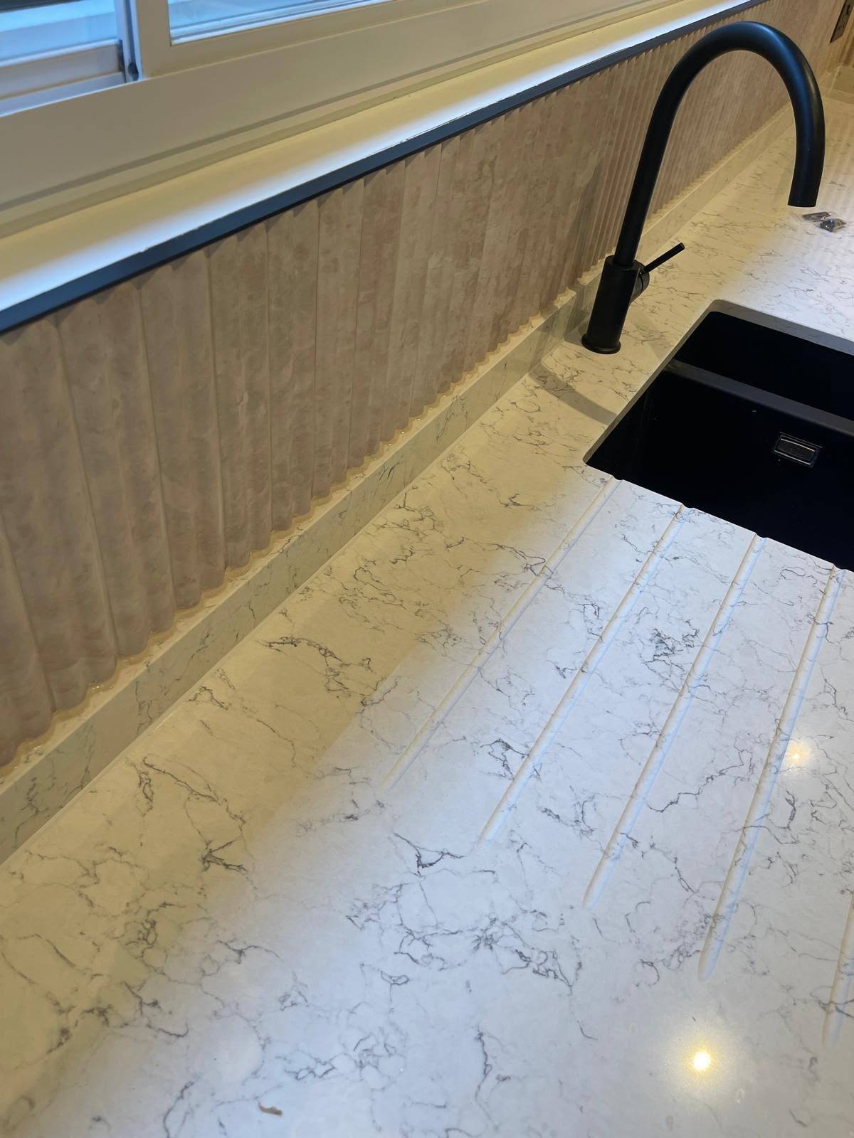 Marble kitchen worktop sealed to a textured splashback around a black sink