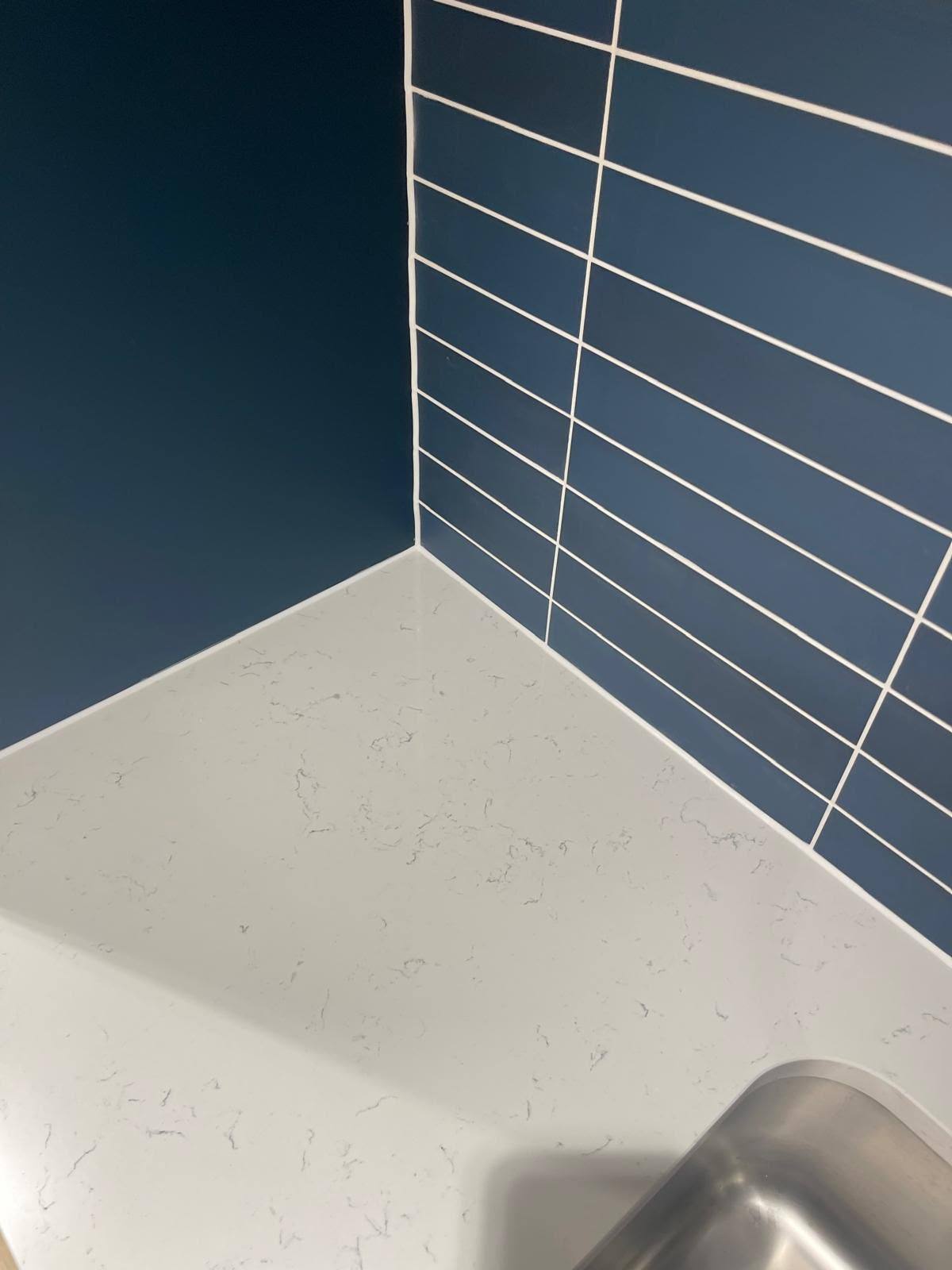 Marble worktop corner sealed against dark blue tiled kitchen walling