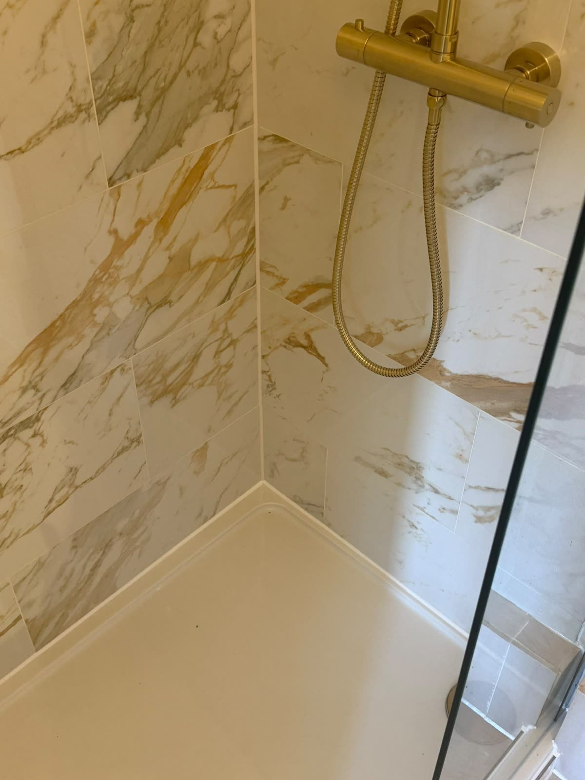 Neat white silicone bead around a shower tray perimeter against gold-veined marble tiles