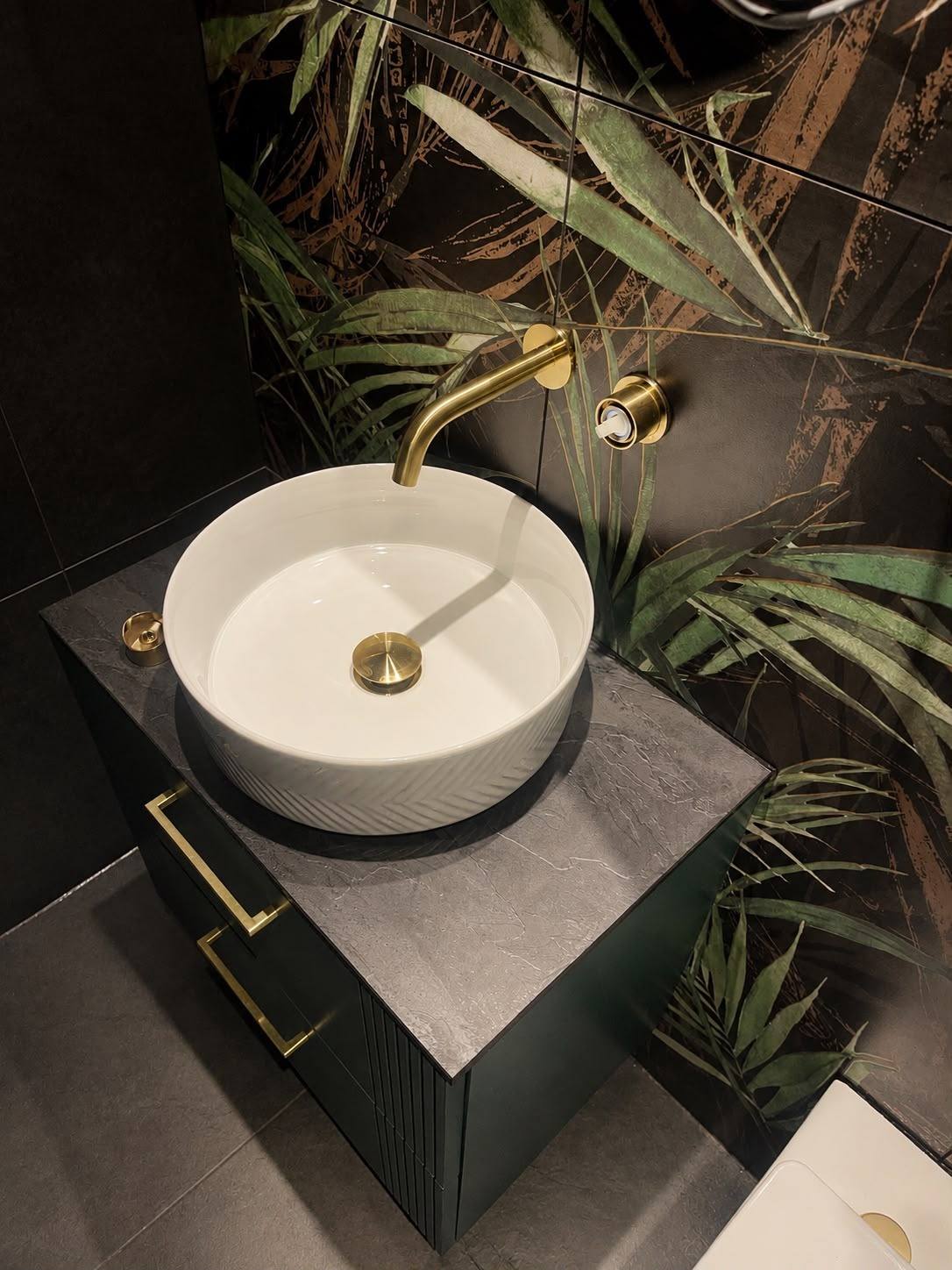 Vessel basin and dark vanity sealed against a wallpapered bathroom wall