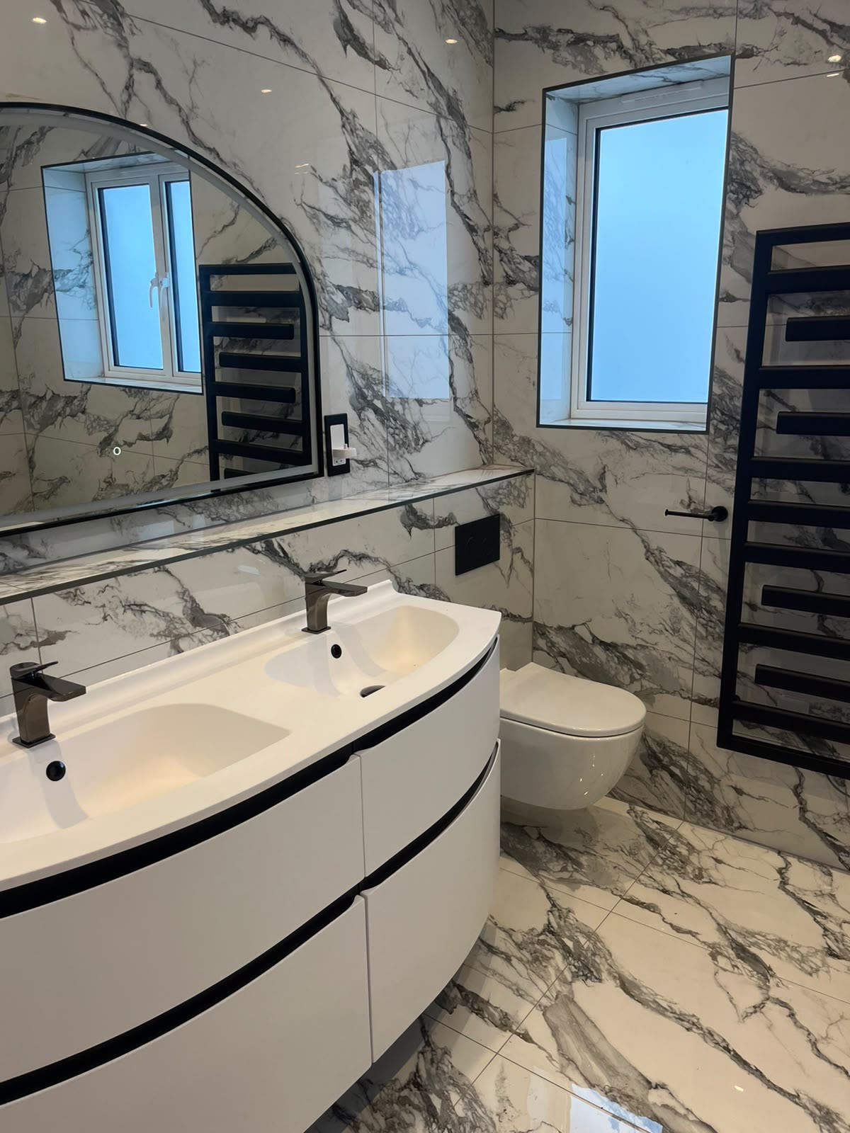Marble bathroom with curved double vanity and wall-hung WC neatly silicone sealed