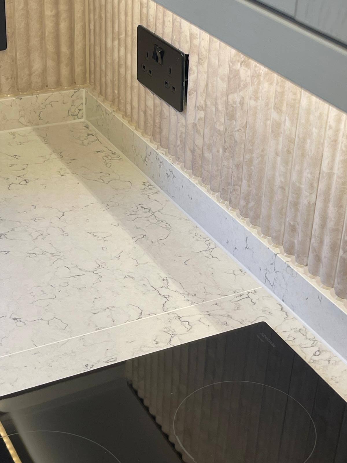 Crisp white silicone sealant line where a marble kitchen worktop meets a fluted splashback
