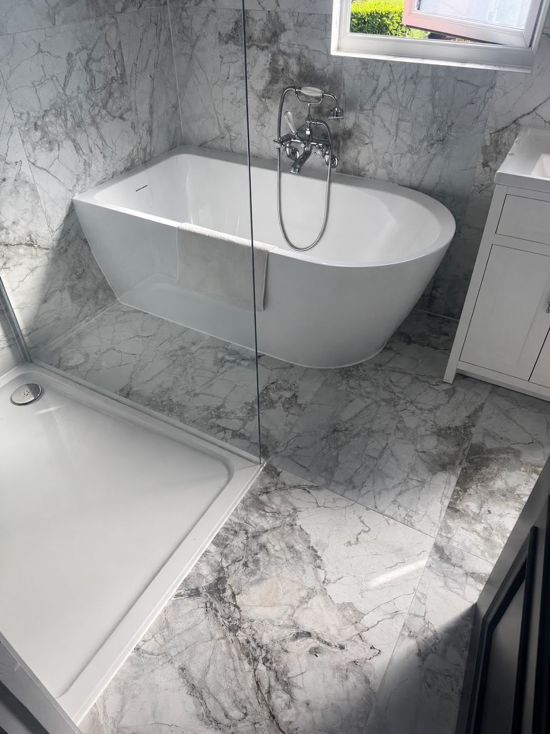 Marble-tiled bathroom with freestanding bath and shower tray ready for silicone sealing in Kent