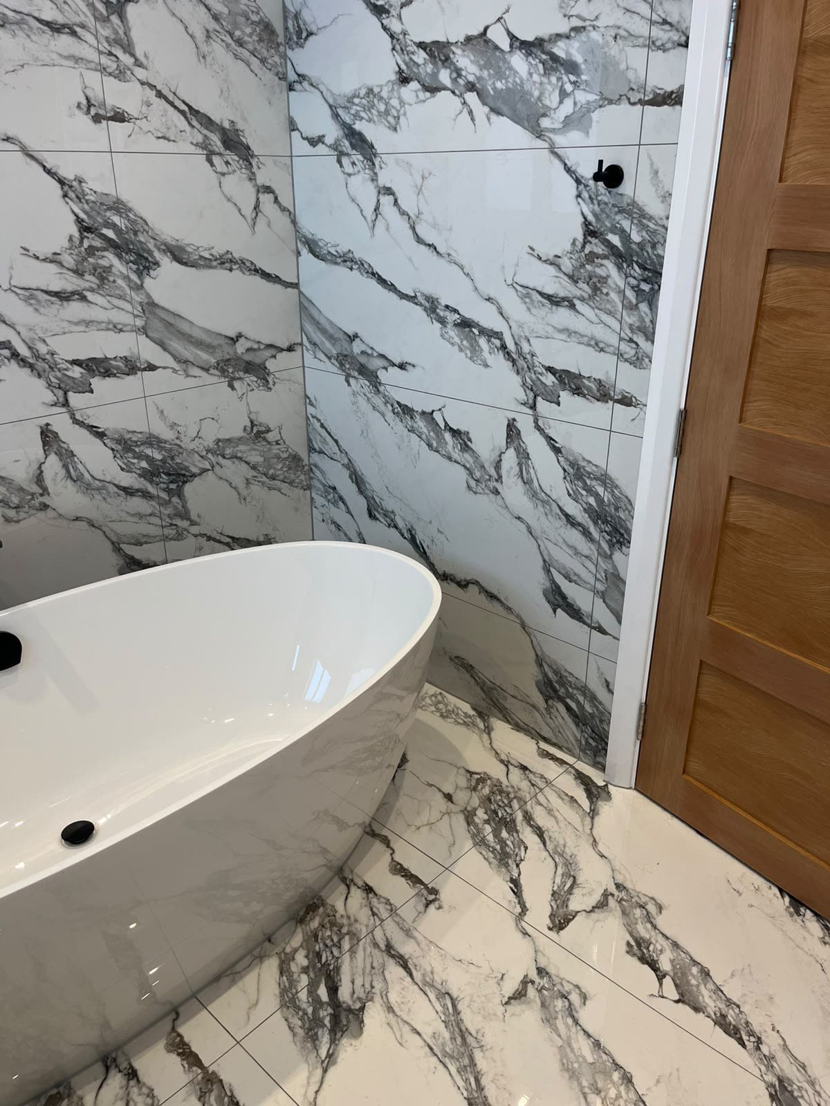Freestanding bath on marble-effect tiles with sealed wall-to-floor and door frame joints