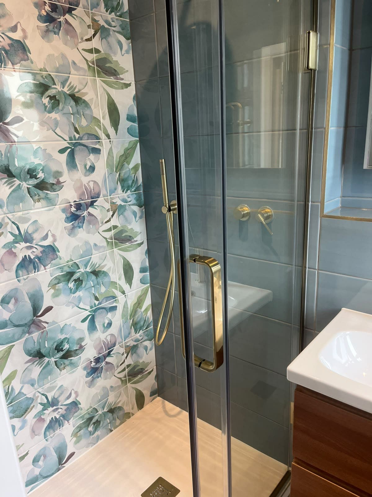 Floral and blue tiled shower enclosure with brass fittings and silicone sealed tray
