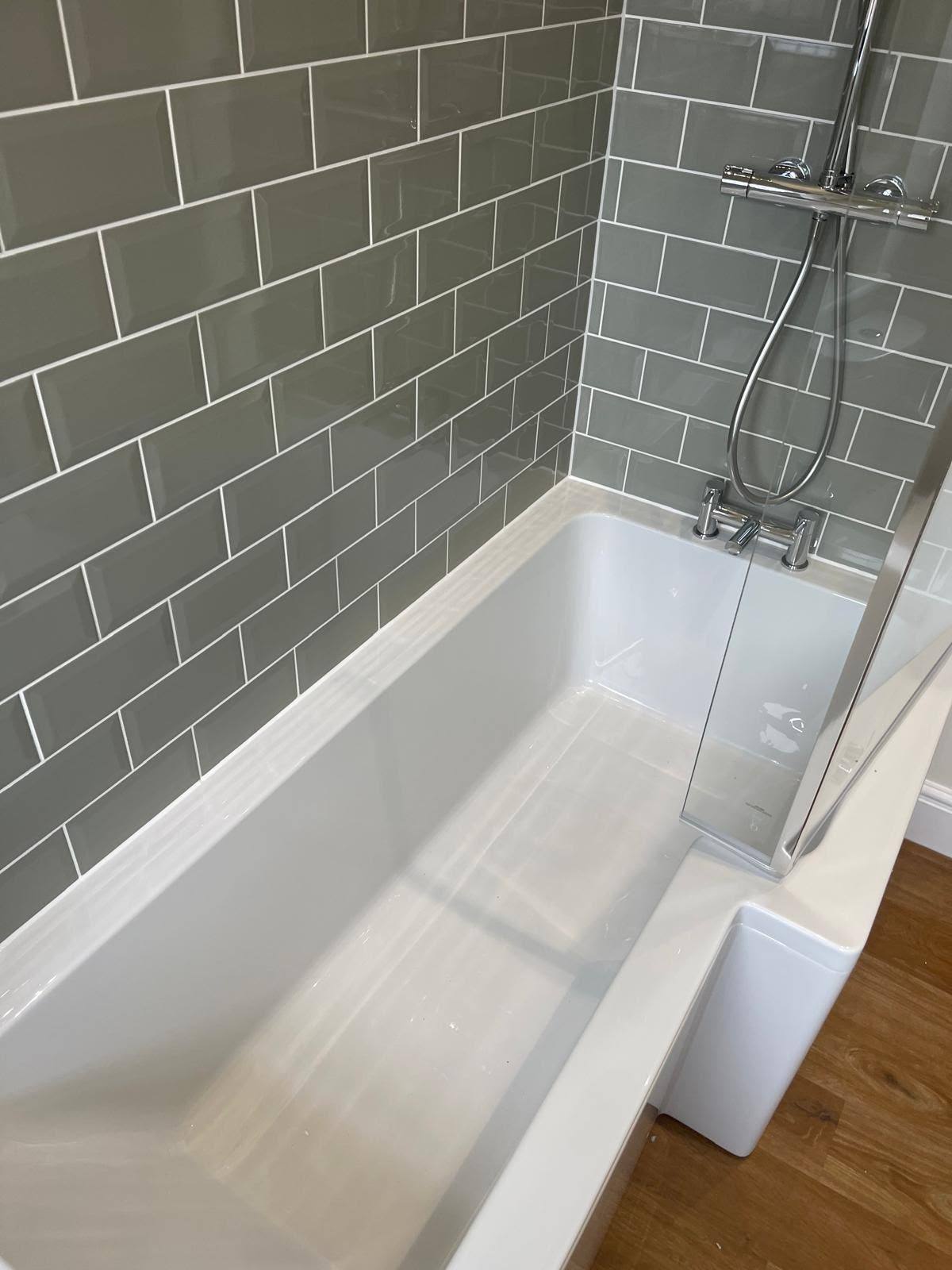 Bath sealed to grey subway tiled walling behind a glass screen