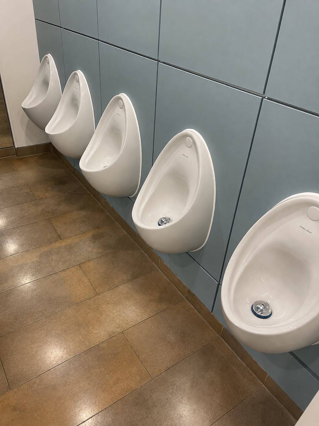 Wall-hung urinals sealed to panelled walling in a commercial washroom