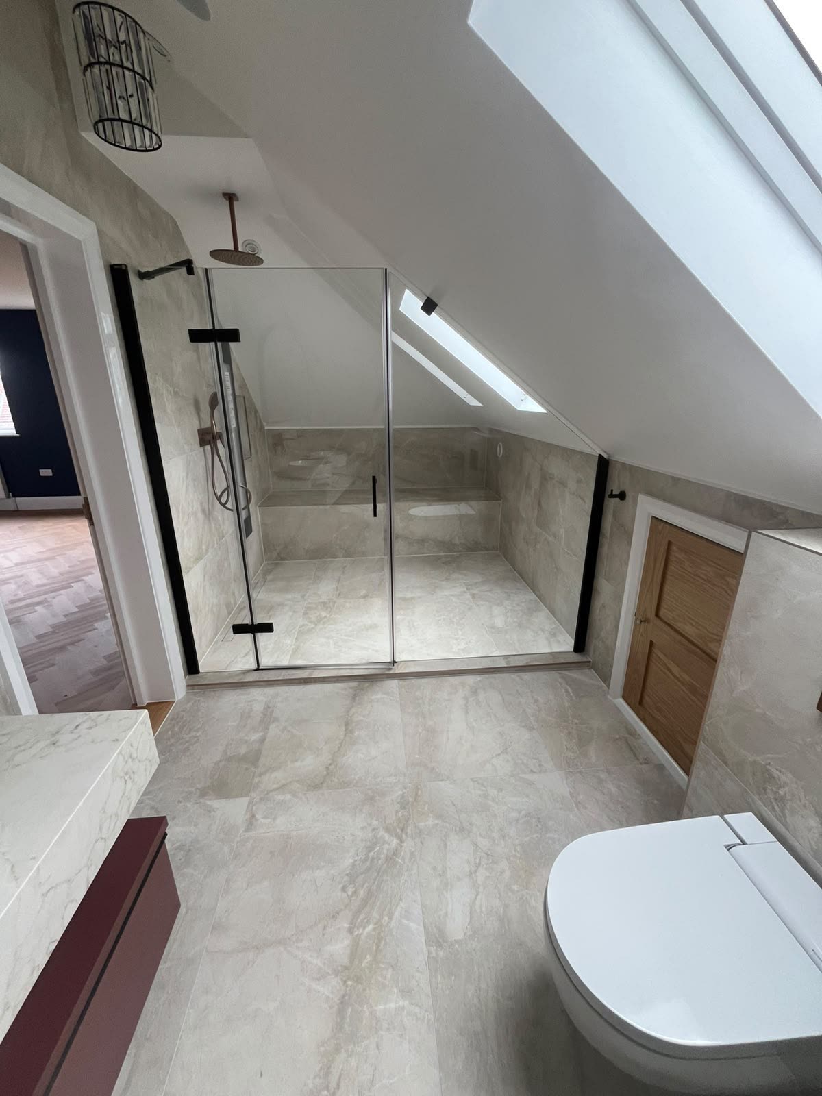 Loft bathroom walk-in shower with glass screen sealed to stone-effect tiled floor