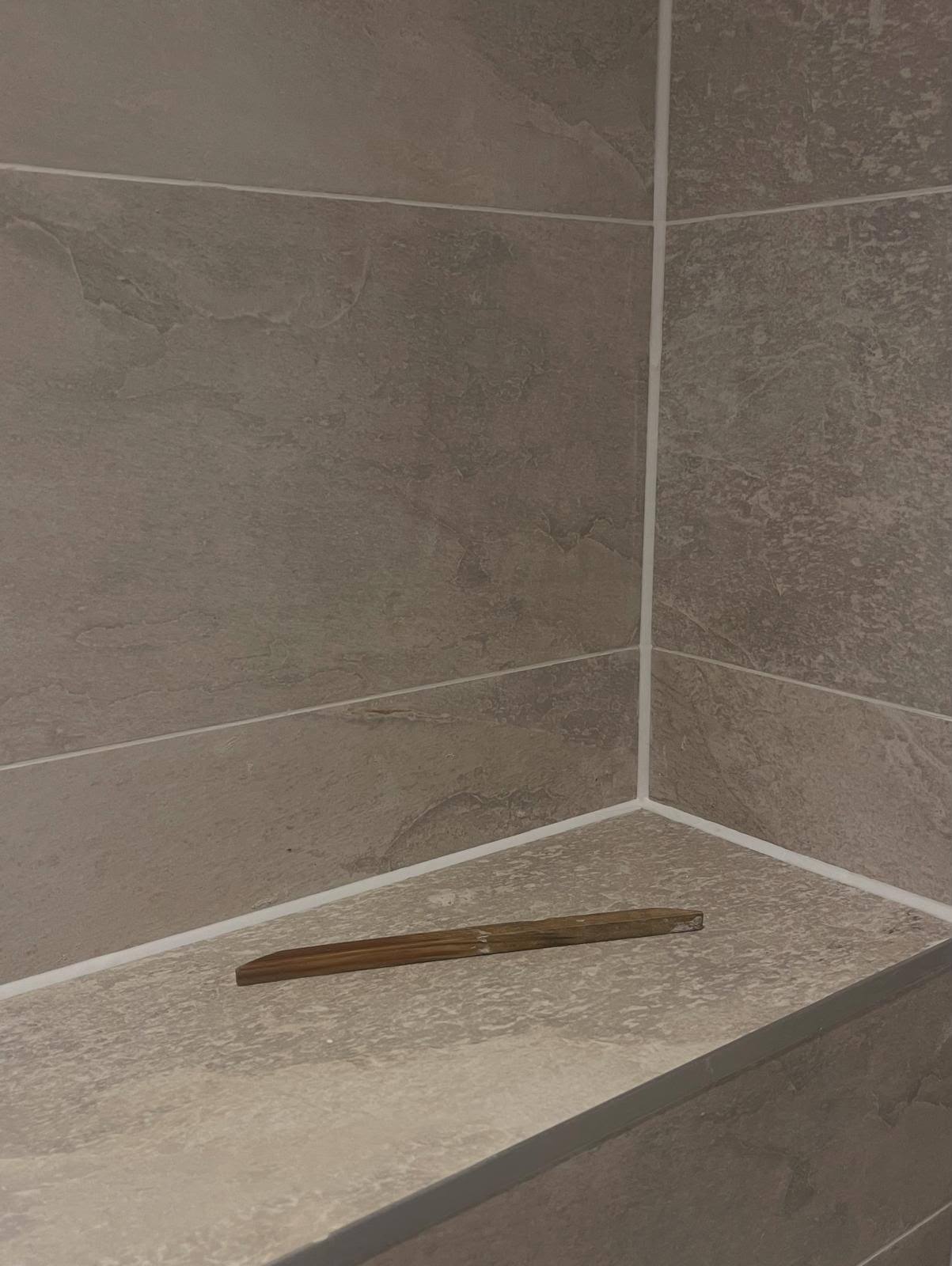 Fresh white silicone replacing old sealant in a stone tiled corner