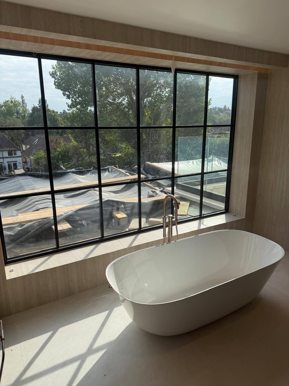 Freestanding bath silicone sealed to tiled flooring beside a full-height window